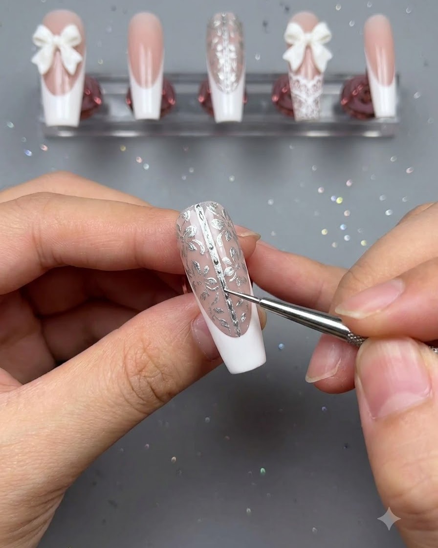 Ein Detailpinsel und eine Pinzette werden verwendet, um winzige Perlenakzente entlang der Mittellinie eines verzierten Blumen-Press-on Nagels zu platzieren.