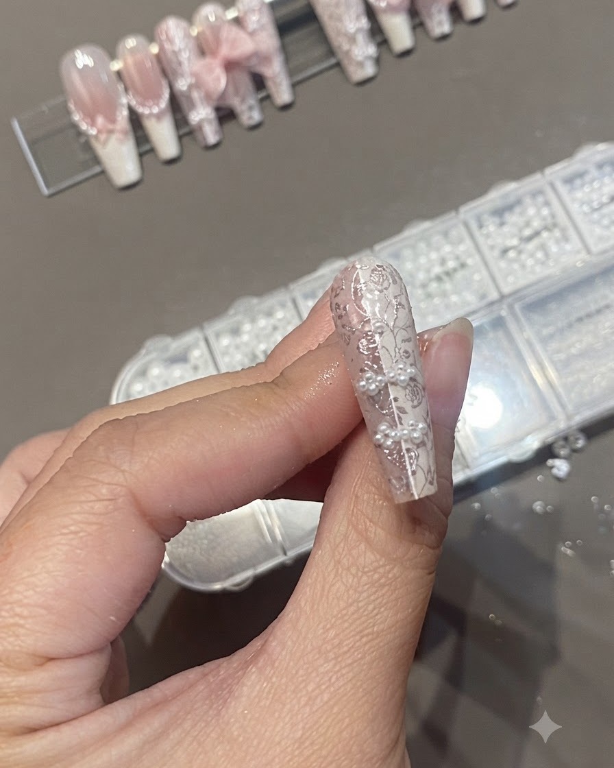 Ein Nagelpinsel trägt einen klaren Überzugslack auf ein strukturiertes Nageldesign mit Perlen und Spitzenstamping auf.