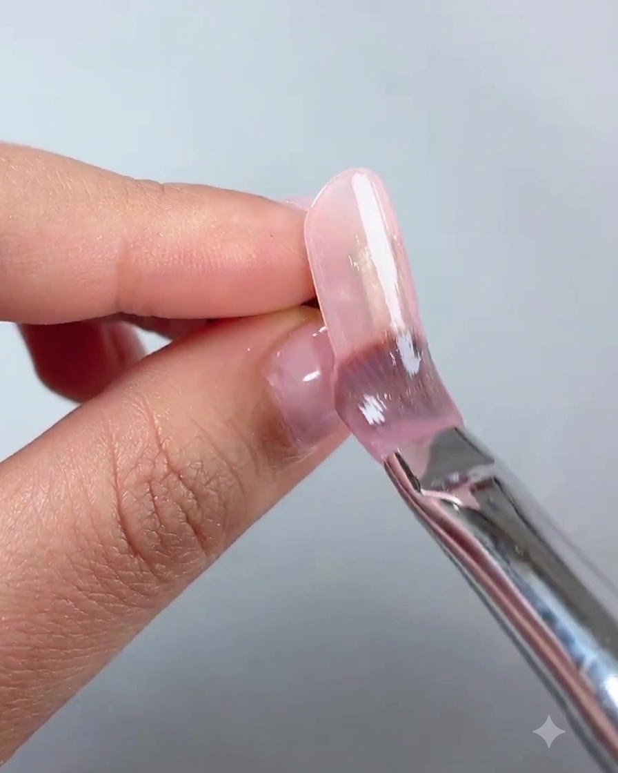 Eine Nahaufnahme eines Fingers mit einer glatten, glänzenden, ausgehärteten Nude-Pink-Grundierung auf einem verlängerten Nagel.