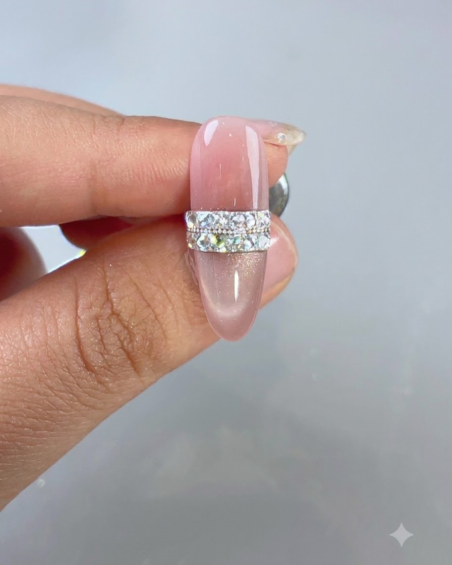 Ein fertiges rosa Cat-Eye-Nageldesign mit einem funkelnden Strass- und Perlenringmotiv unter Studiolicht.
