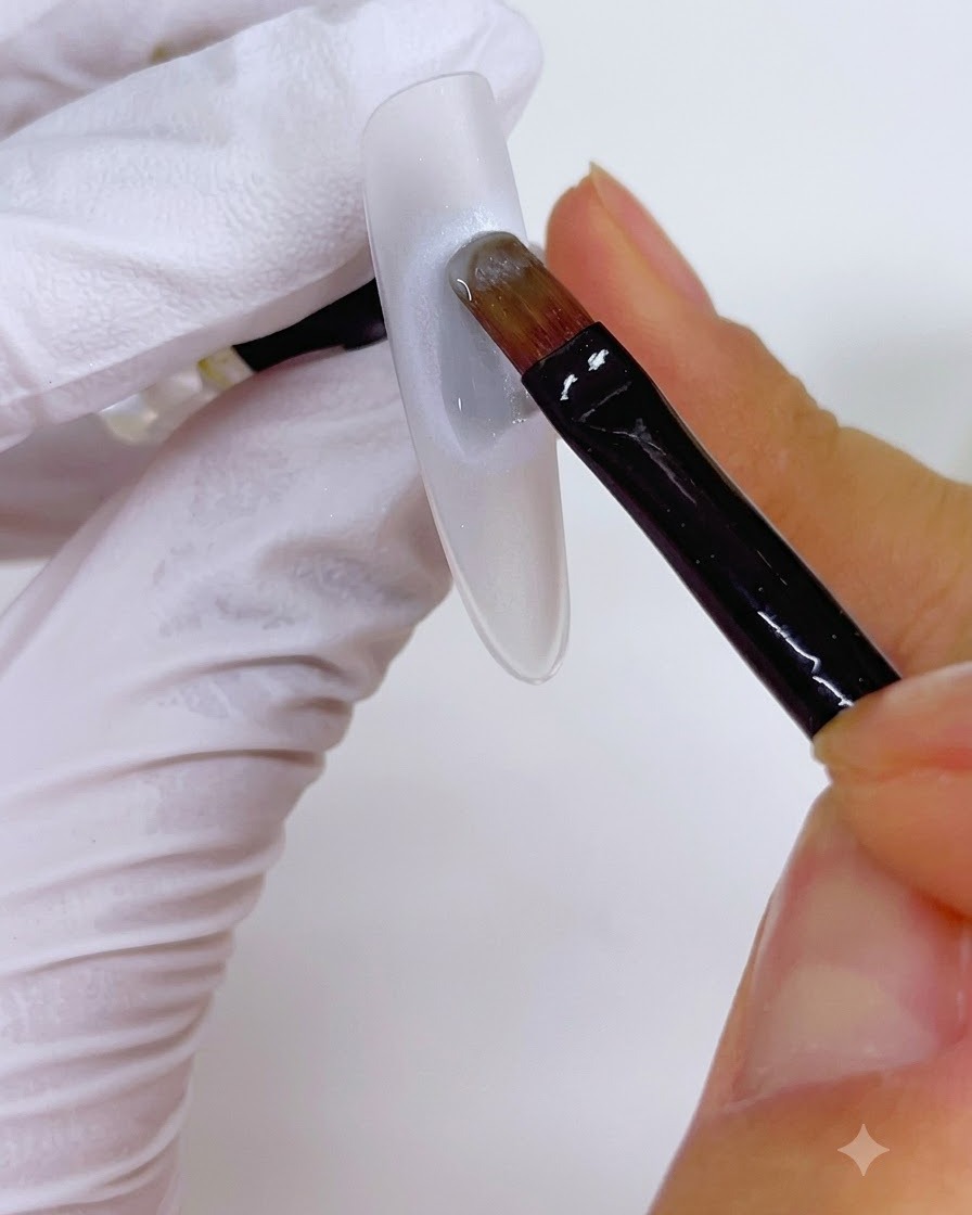 Ein Pinsel trägt eine Gelschicht über eine kreisförmige Perlenbasis auf einem Nagel auf.