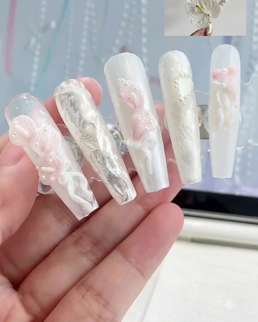 Ein Display-Ständer hält mehrere Press-On-Nägel mit verschiedenen 3D-weißen und rosa floralen Nagelkunst-Designs.