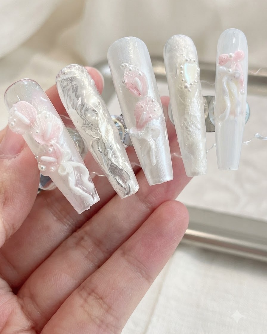 Eine Präsentation fertiger Press-On-Nägel mit 3D-Calla-Lilien, Schleifen und Perlenverzierungen auf neutralem Hintergrund.