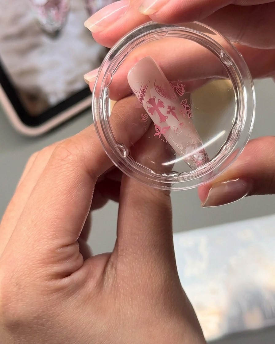 Ein klarer Jelly-Stamper überträgt rosa gestempelte Nagelkunst-Designs auf eine mandelförmige Nageloberfläche.