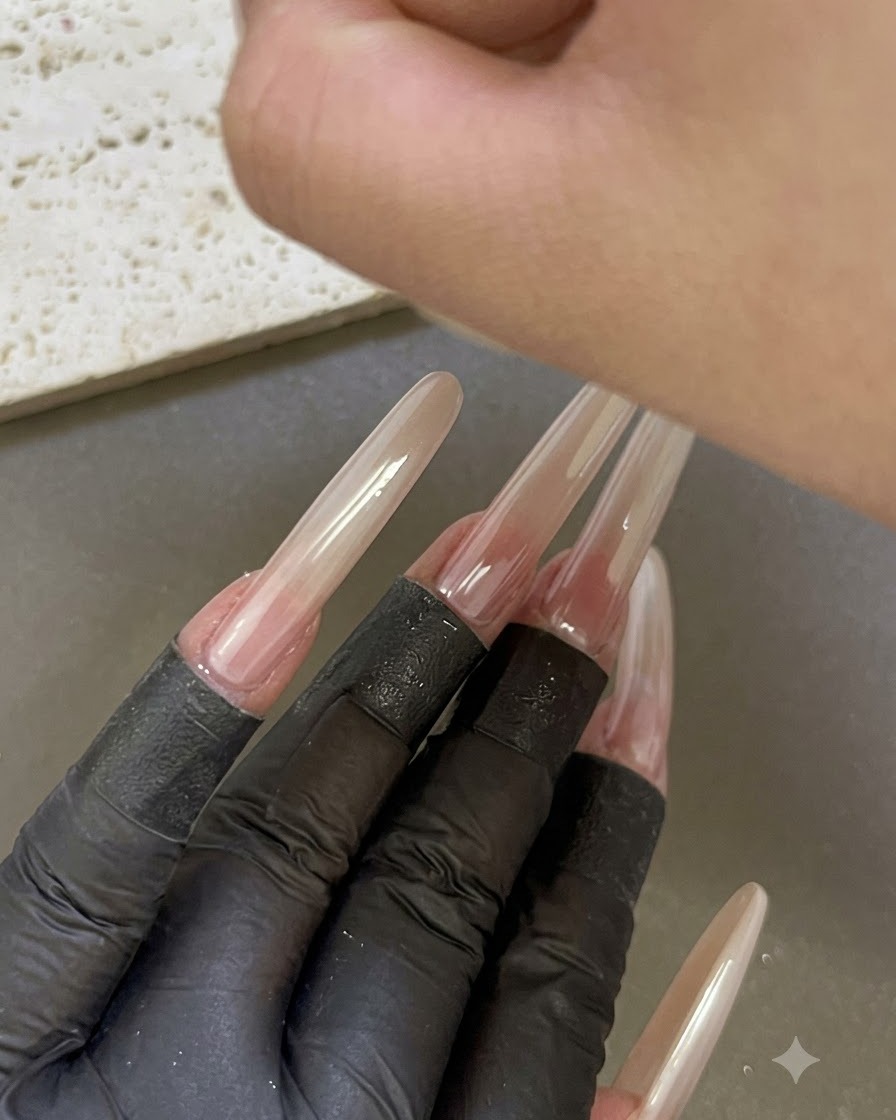 Eine Hand unter einer UV-/LED-Nagellampe platziert, mit anderen manikürten verlängerten Fingern im Vordergrund.