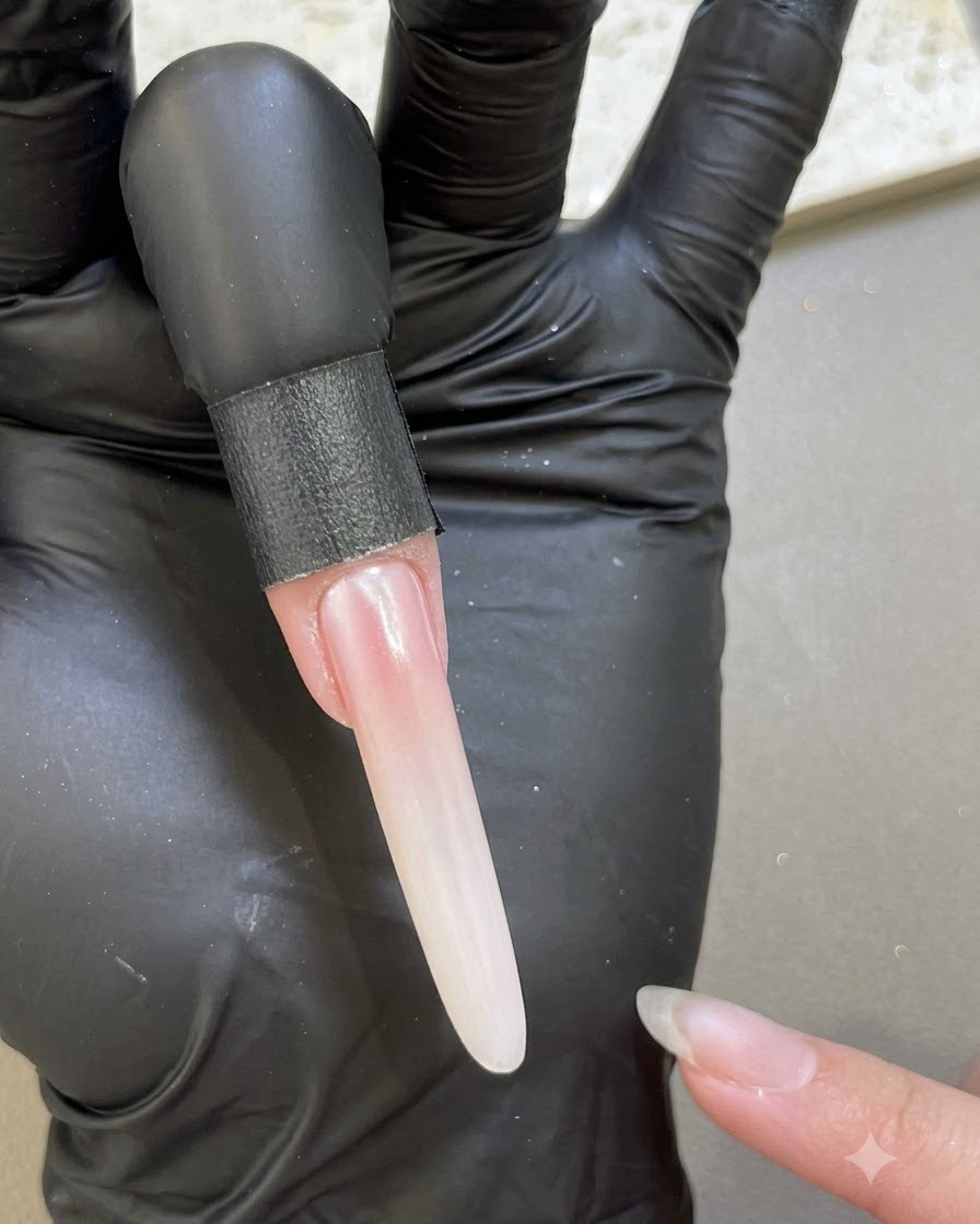 Ein verlängerter Nagel zeigt ein glattes, perlmuttrandiges Finish nach dem Versiegeln mit Base-Gel an den Rändern.
