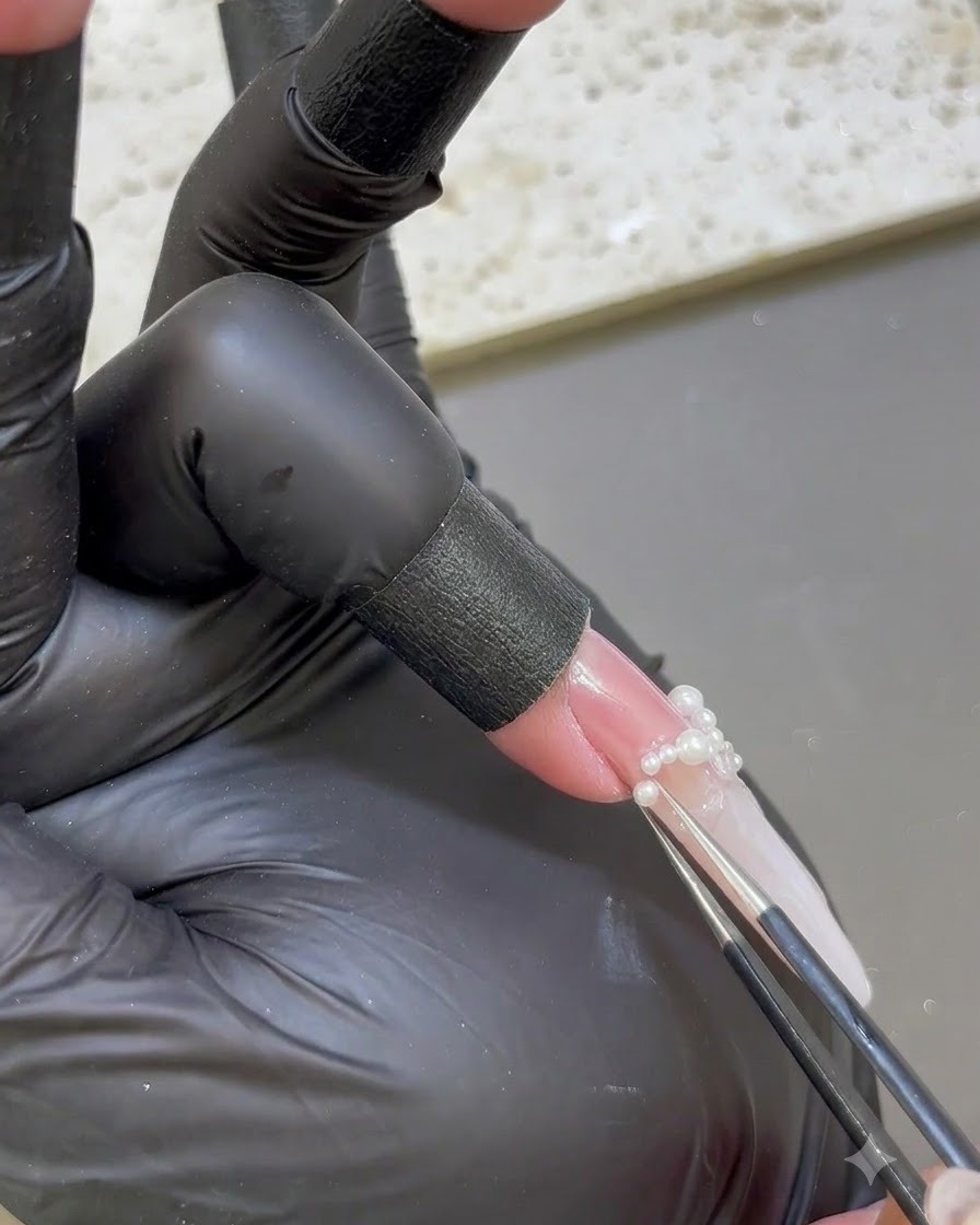 Präzisionspinzette platziert winzige weiße Perlen auf der Basis eines verlängerten Nagels.