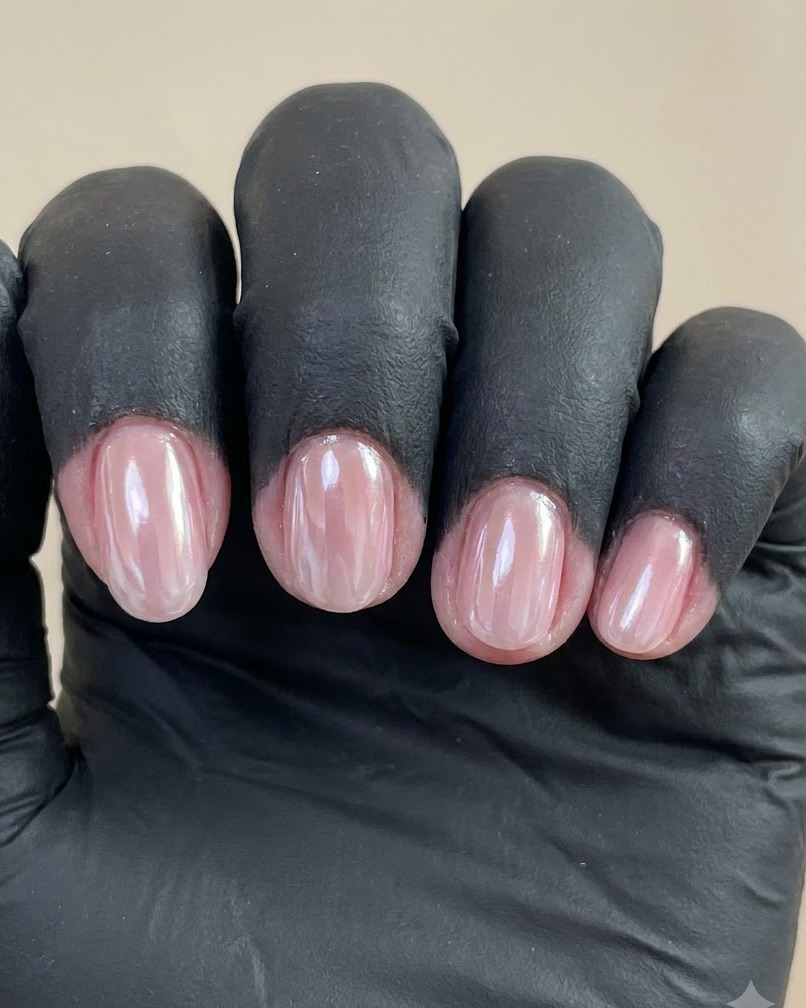 Nahaufnahme einer behandschuhten Hand mit vier manikürten Nägeln mit glänzendem Pearl-Chrome-Finish vor einem schlichten Hintergrund.