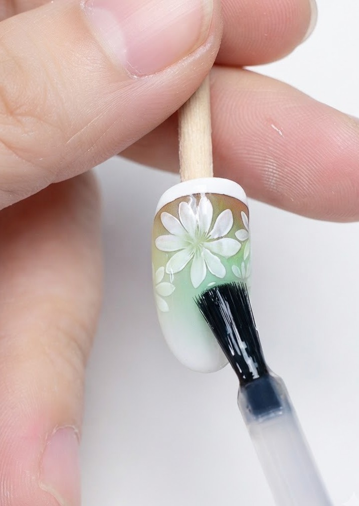 Ein Pinsel trägt matten Top Coat über die fertige Gänseblümchen-Nagelkunst auf.