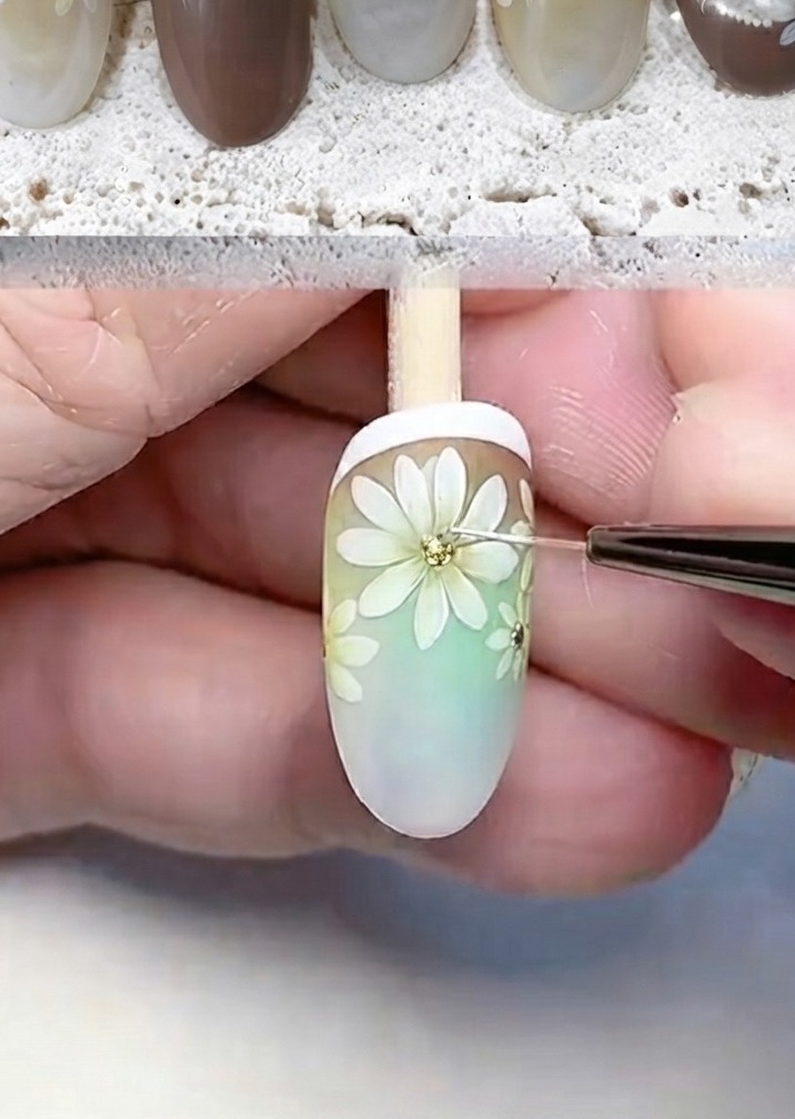 Ein feines Werkzeug fügt Glitzer und weiße Punkte zur Mitte einer gemalten Gänseblümchenblüte hinzu.
