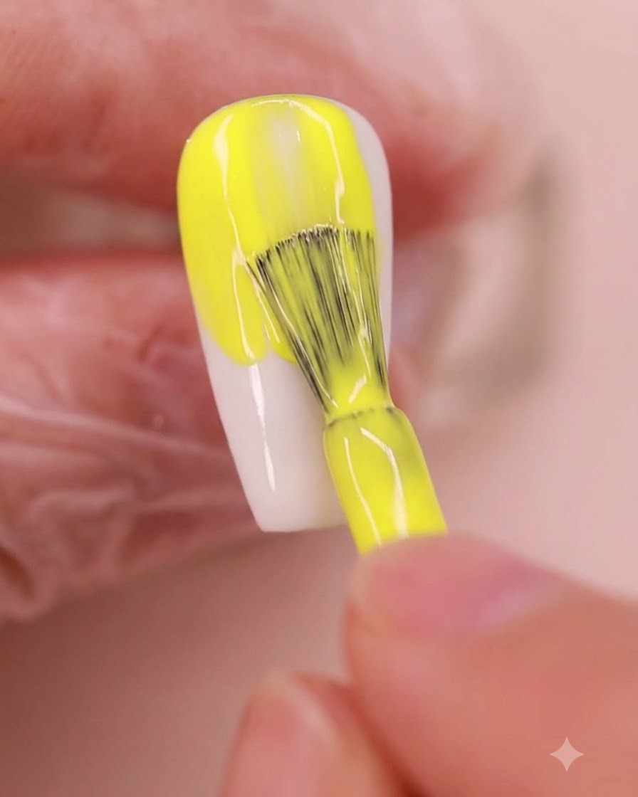 Ein Nagelpinsel trägt eine leuchtend gelbe Gelpolitur gleichmäßig auf eine mandelförmige Nagelplatte auf.