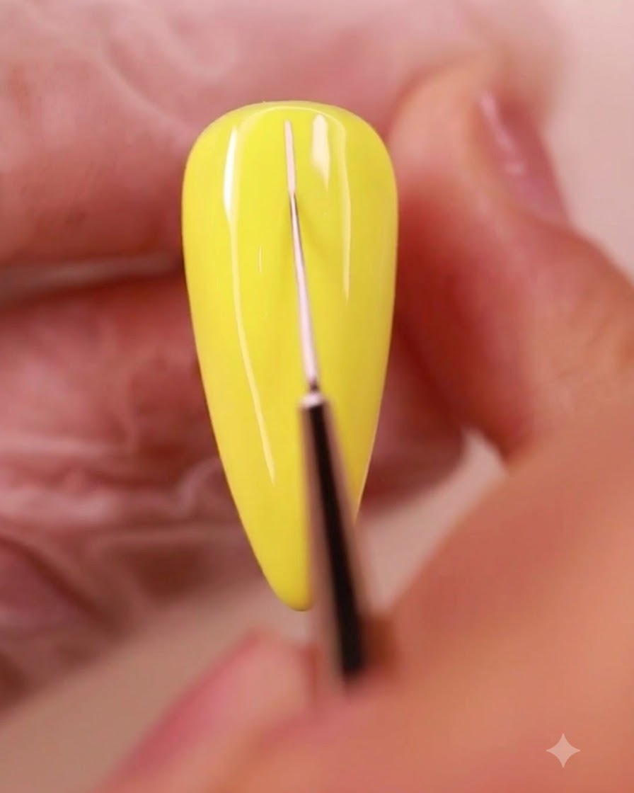 Ein feiner Liner-Pinsel zeichnet dünne weiße Hilfslinien über eine gelb lackierte Nageloberfläche.