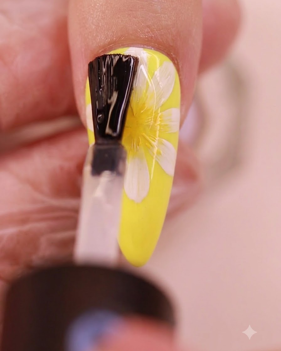 Ein Pinsel trägt eine klare Schicht No-Wipe Topcoat über das gemalte Gänseblümchen-Nageldesign auf.