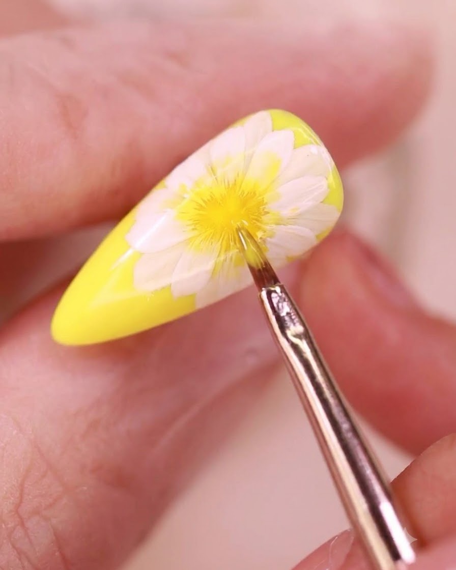 Ein feiner Detailpinsel trägt einen klaren Topcoat über ein Blumen-Nageldesign auf.
