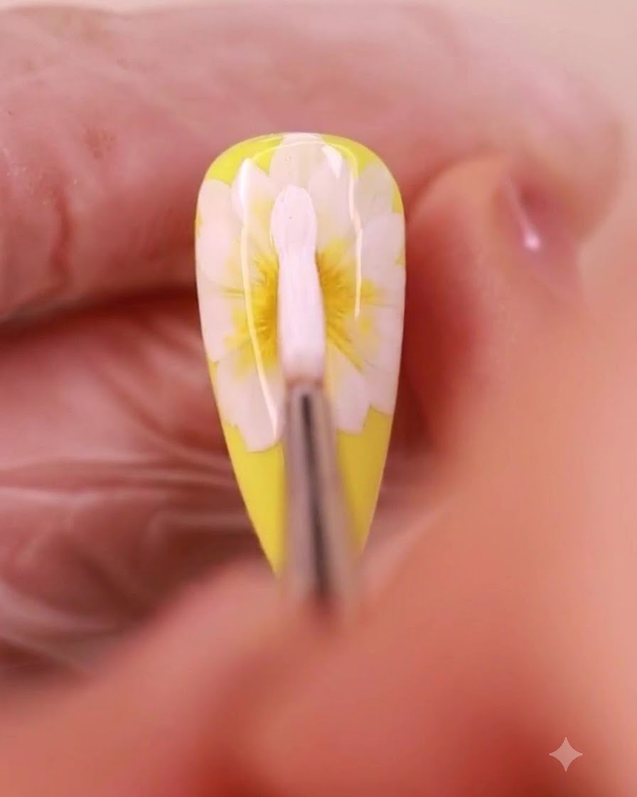 Ein Nagelkunstpinsel trägt weißes Gel auf, um eine dritte Schicht Blütenblätter auf einem Gänseblümchen-Design zu bilden.