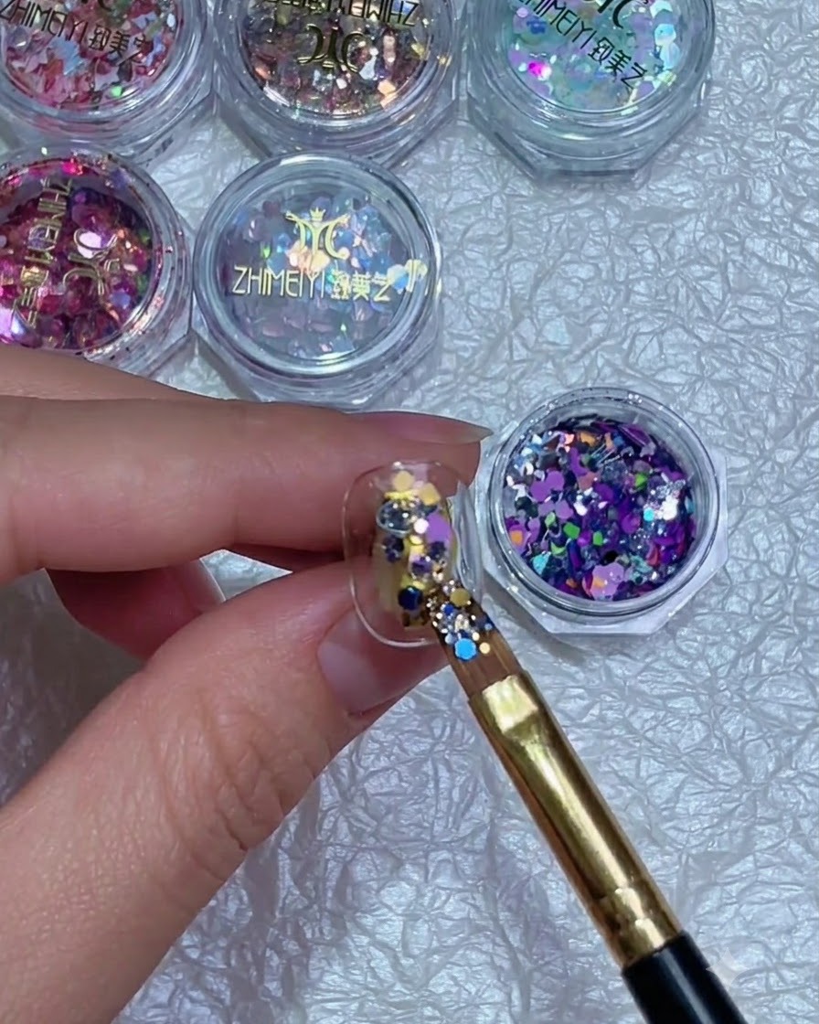 Ein Pinsel, der die Position bunter Glitterflocken auf einem Fingernagel präzise anpasst.