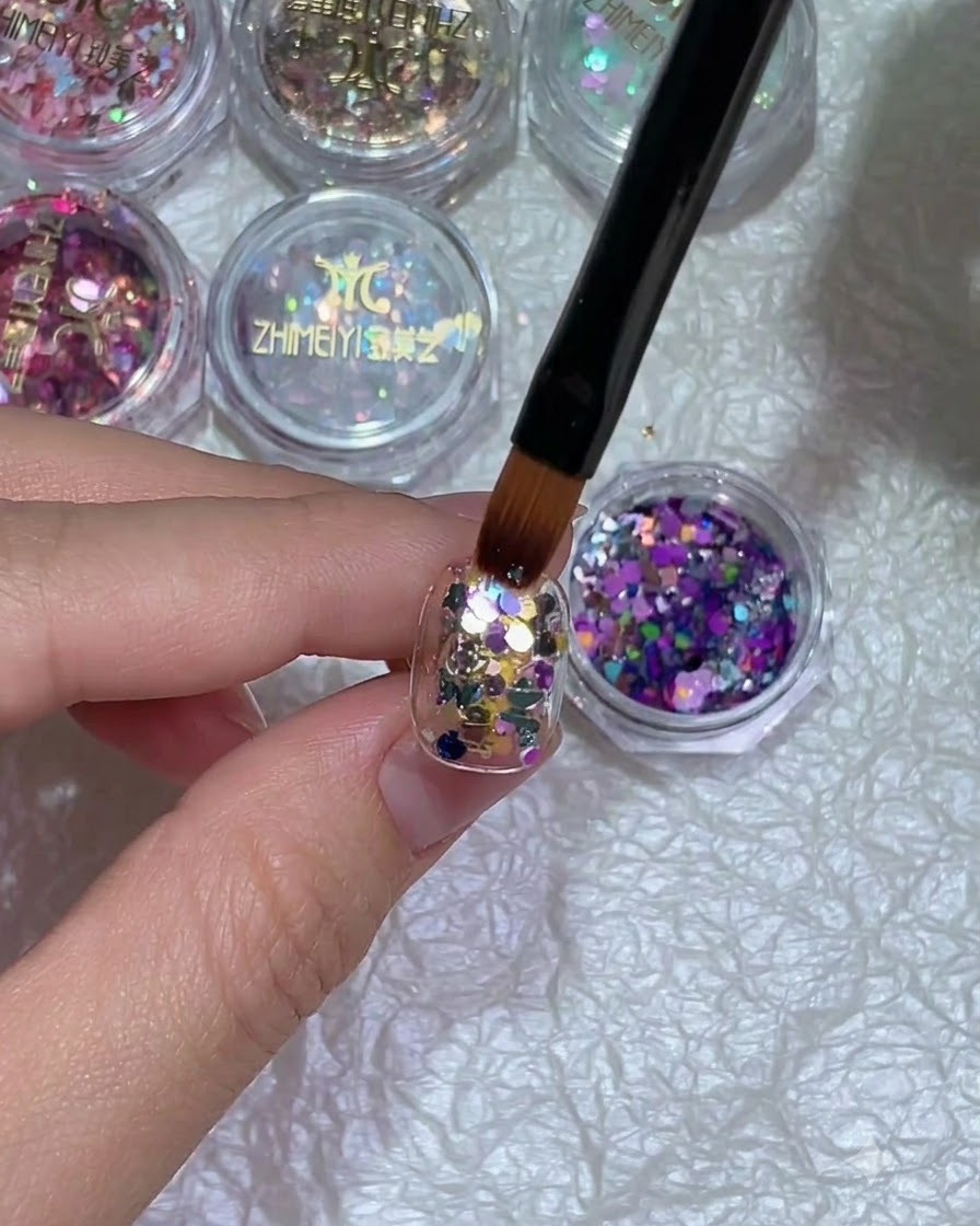 Eine Nahaufnahme einer Hand mit Glitter-Nageldesign unter einer Aushärtungslampe.