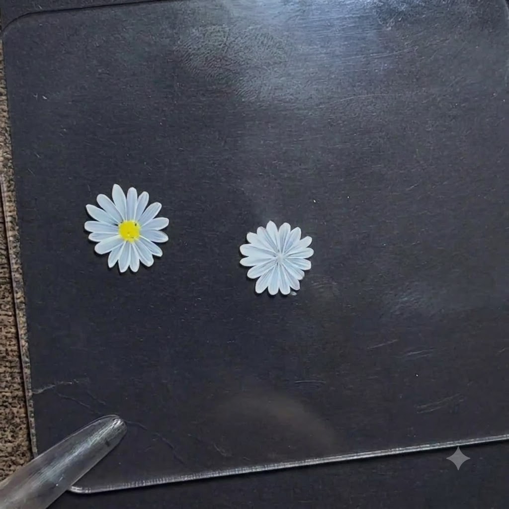 Ein Dotting-Pen trägt einen kleinen Punkt aus leuchtend gelbem Gel auf die Mitte einer weißen Gänseblümchen-Blume auf einem dunklen Display-Board auf.