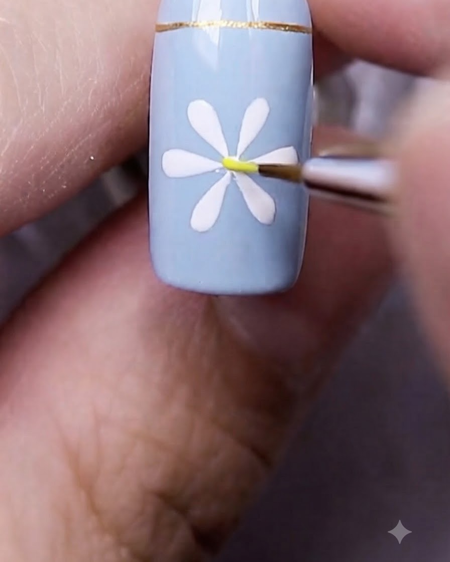 Ein feiner Nail-Art-Pinsel setzt einen winzigen gelben Punkt direkt in die Mitte des gemalten weißen Gänseblümchens.