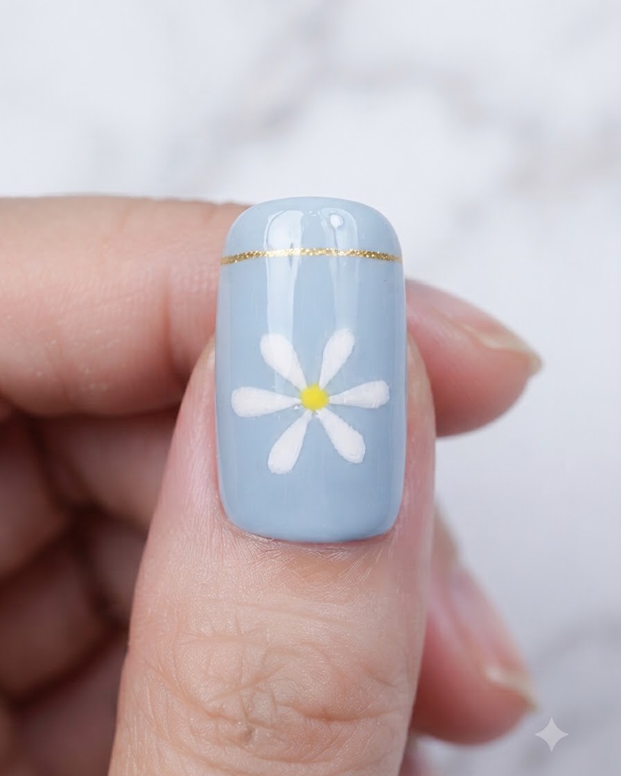 Ein Pinsel trägt einen klaren, glänzenden Überlack über einen fertigen blauen Nagel mit Gänseblümchen-Design auf.