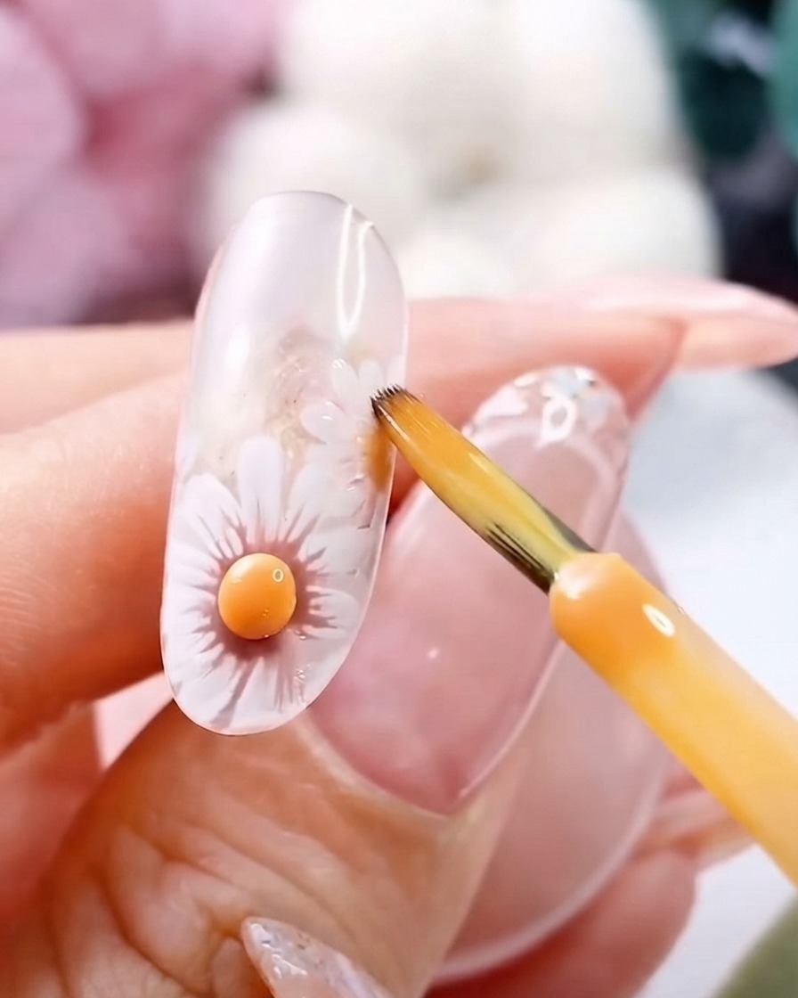 Ein feiner Pinsel in der Nähe einer ausgehärteten 3D gelben Blumenmitte auf einem klaren Gelnagel.
