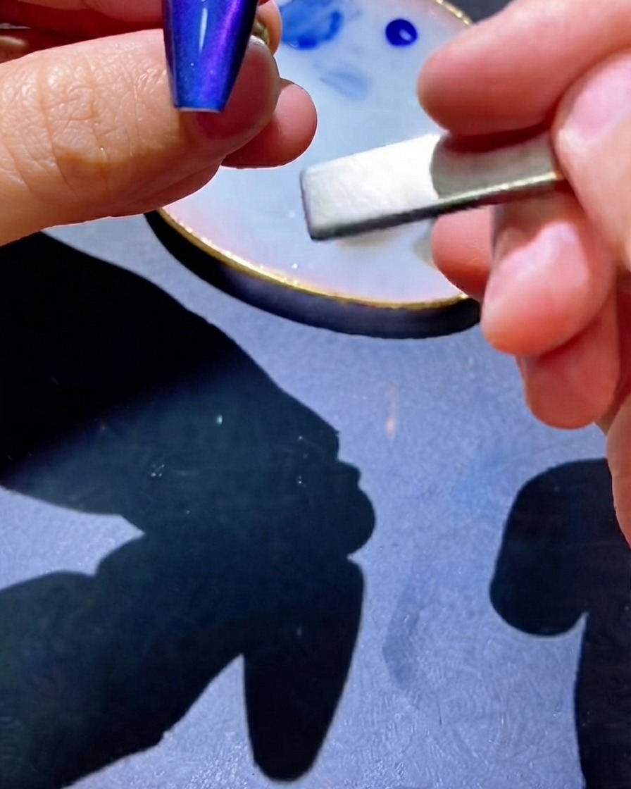 Ein Magnet wird seitlich am Nagel verwendet, um Pigmente in eine zentrierte Linie zu ziehen.