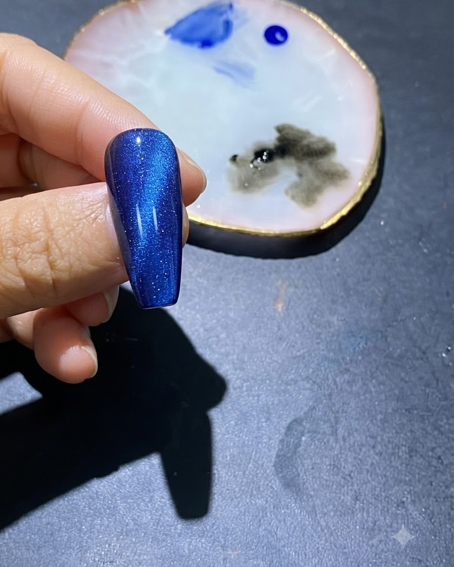 Eine Nahaufnahme eines blauen Cat-Eye Gel-Nagels mit blauen Lackflecken in der Mitte und einer Nagelkunst-Palette in der Nähe.