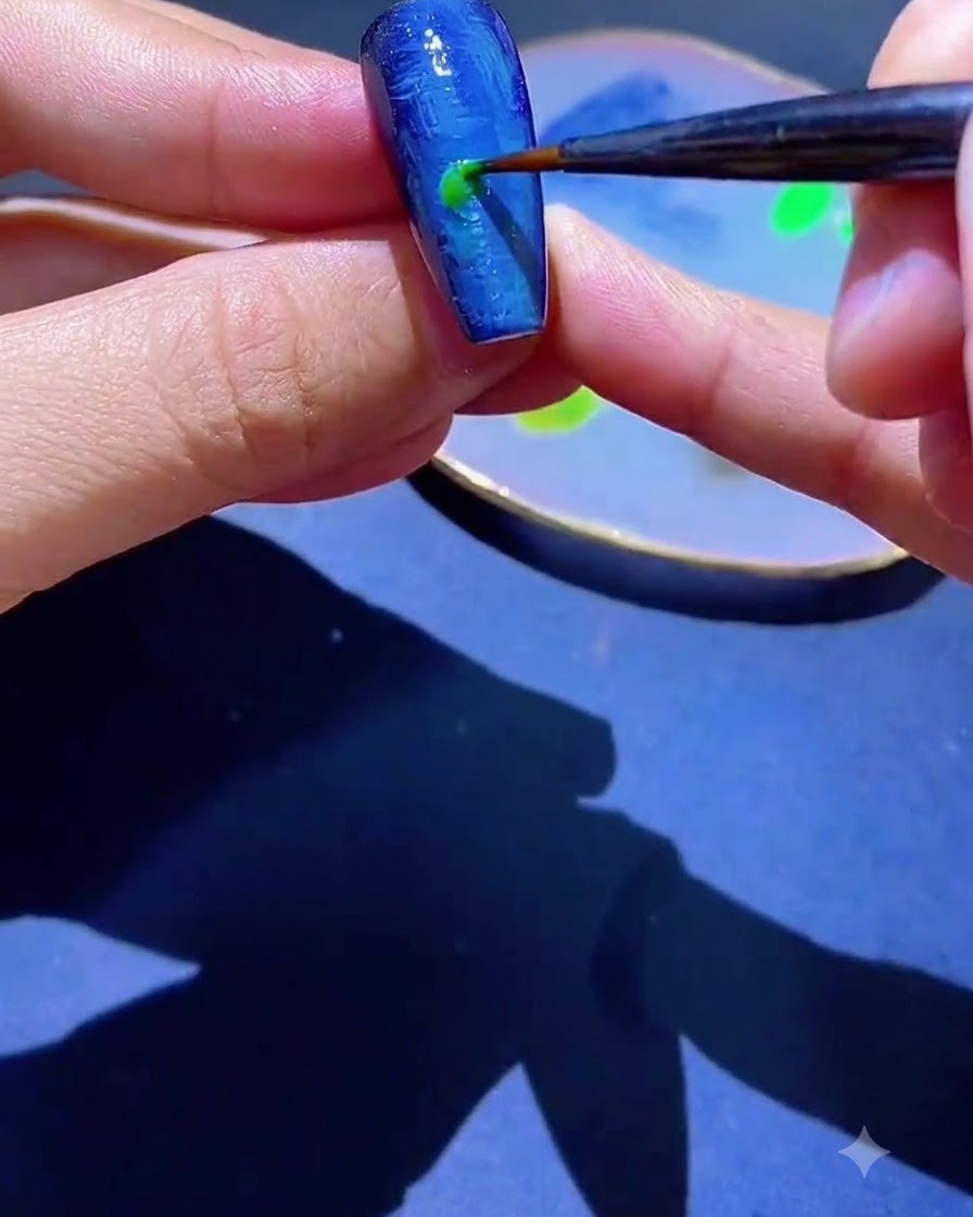 Ein feiner Liner-Pinsel trägt einen Tupfen grünen Gel-Lacks auf einen blau strukturierten Nagel auf.
