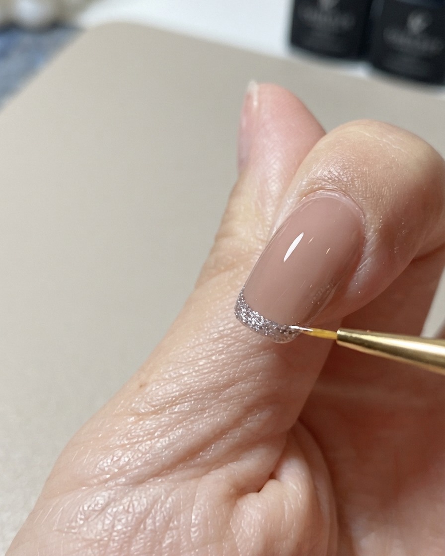 Ein feiner Nail-Art-Liner-Pinsel korrigiert und perfektioniert die Kante eines glitzernden Cat-Eye-Spitzendesigns.