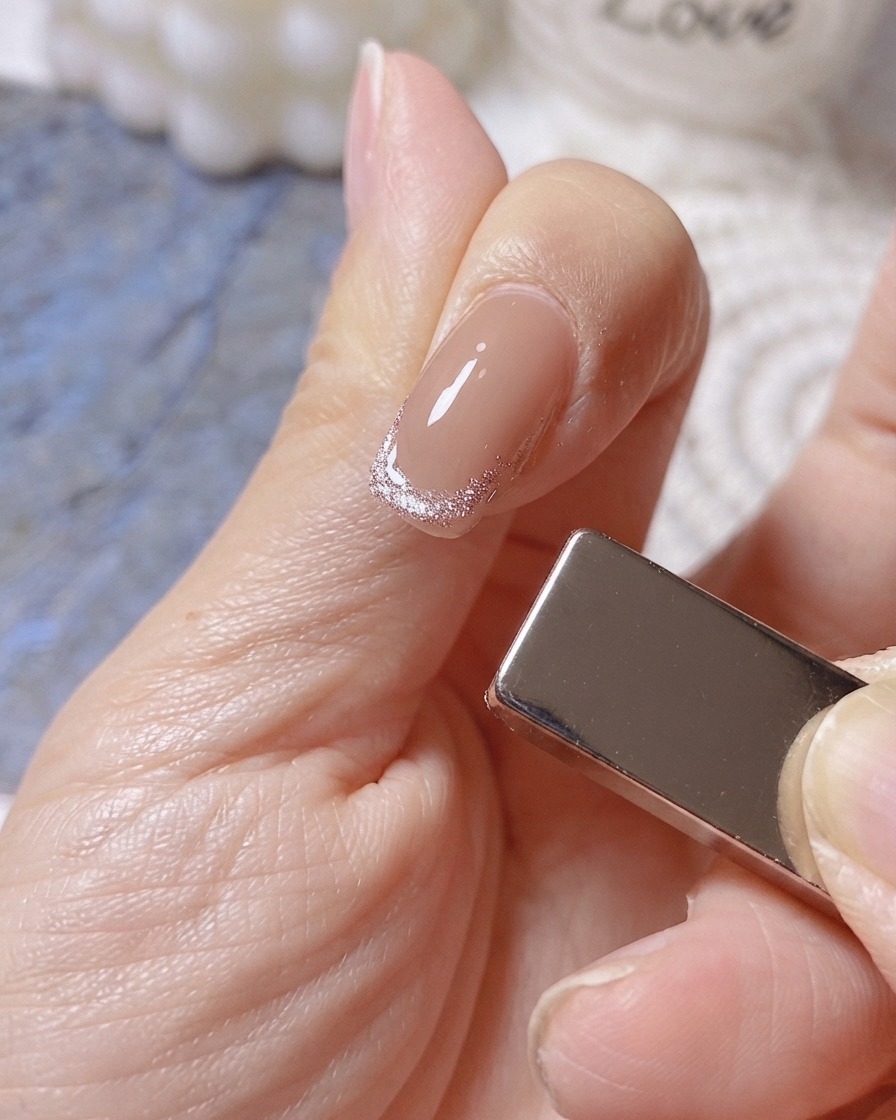 Ein Magnet ist auf der rechten Seite eines Fingers positioniert, um ein breites, leuchtendes Band auf einer Cat-Eye-French-Spitze zu formen.