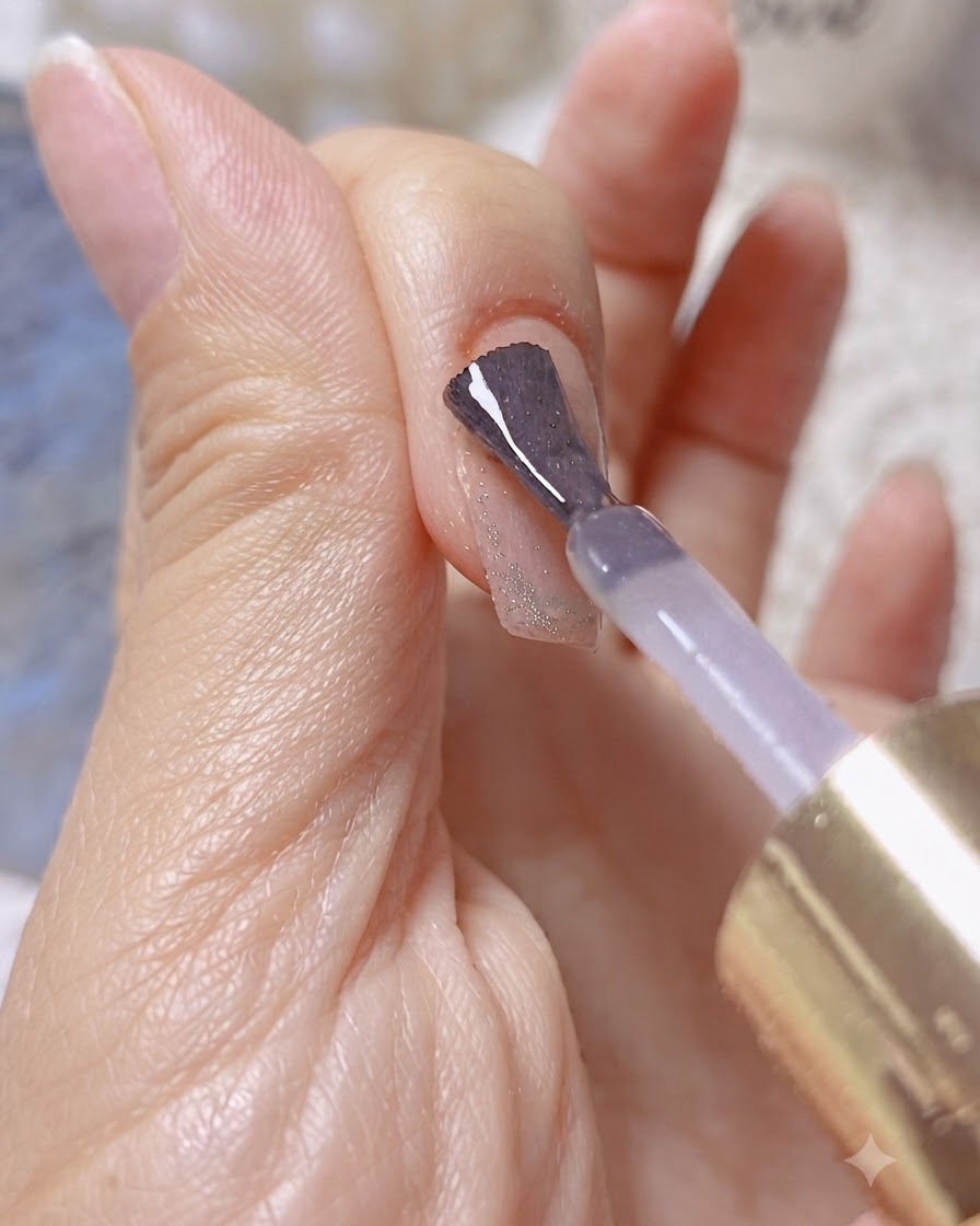 Ein Pinsel trägt klares Aufbau- oder Verstärkungsgel über einem schimmernden Cat-Eye-Nagel auf.