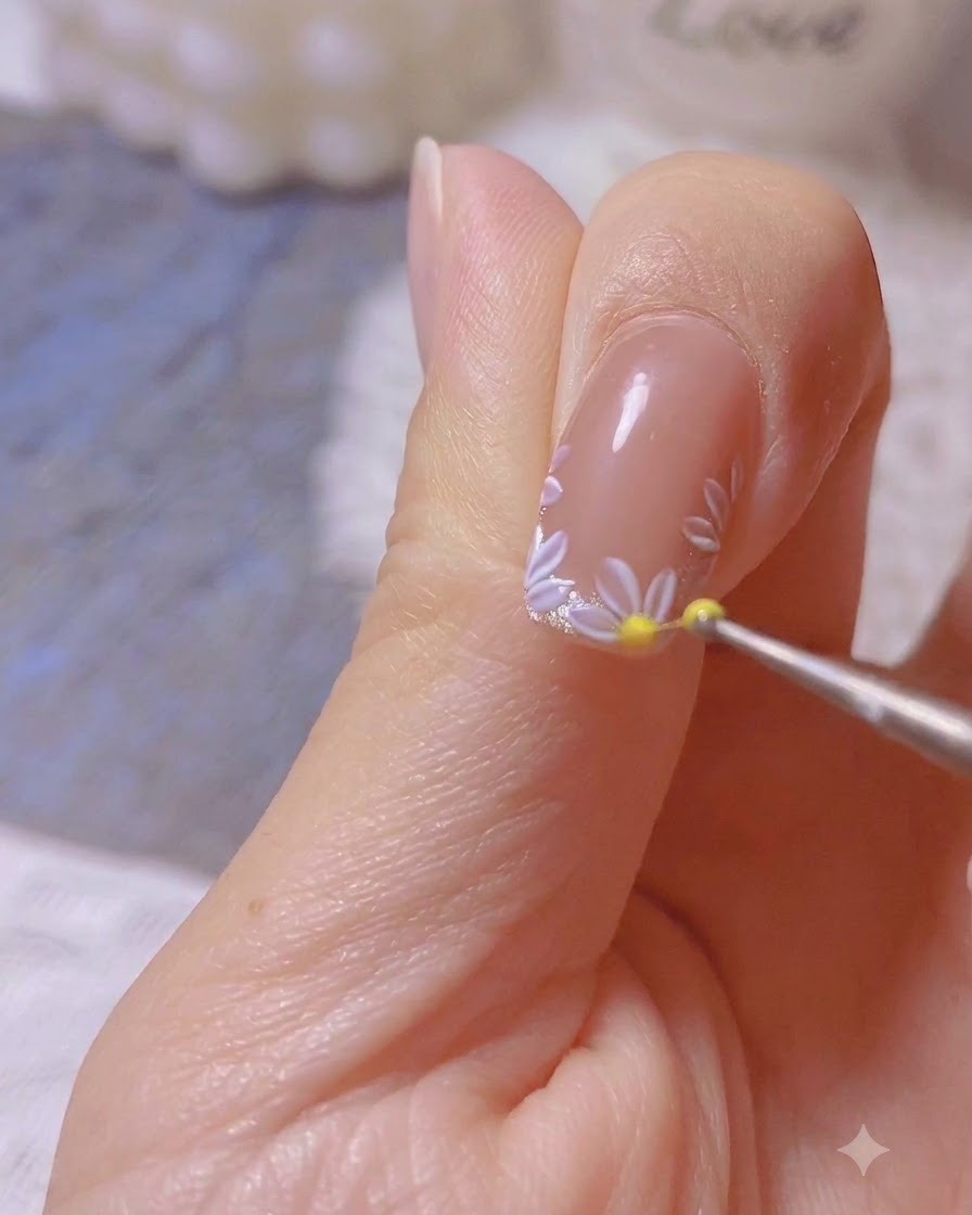 Ein Dotting-Tool platziert einen gelben Punkt in die Mitte eines gemalten weißen Gänseblümchen-Nail-Art-Designs.