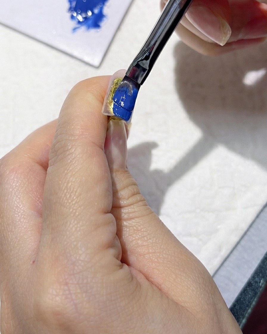 Ein Pinsel, der sorgfältig einen satten dunkelblauen Gel-Nagellack auf einen künstlichen Nagel aufträgt.