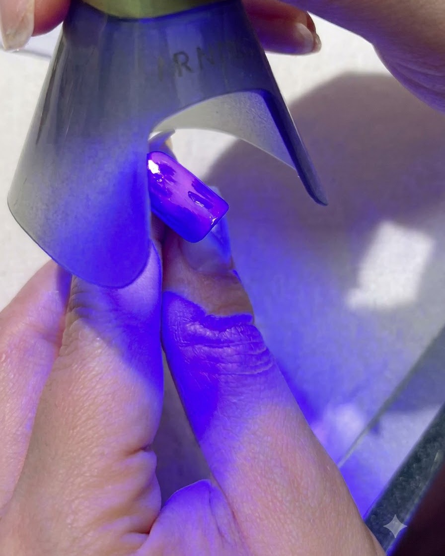 Eine tragbare lila UV-Lampe, die dunkelgrüne Blatt-Nagelkunst auf einem blau lackierten Fingernagel aushärtet.