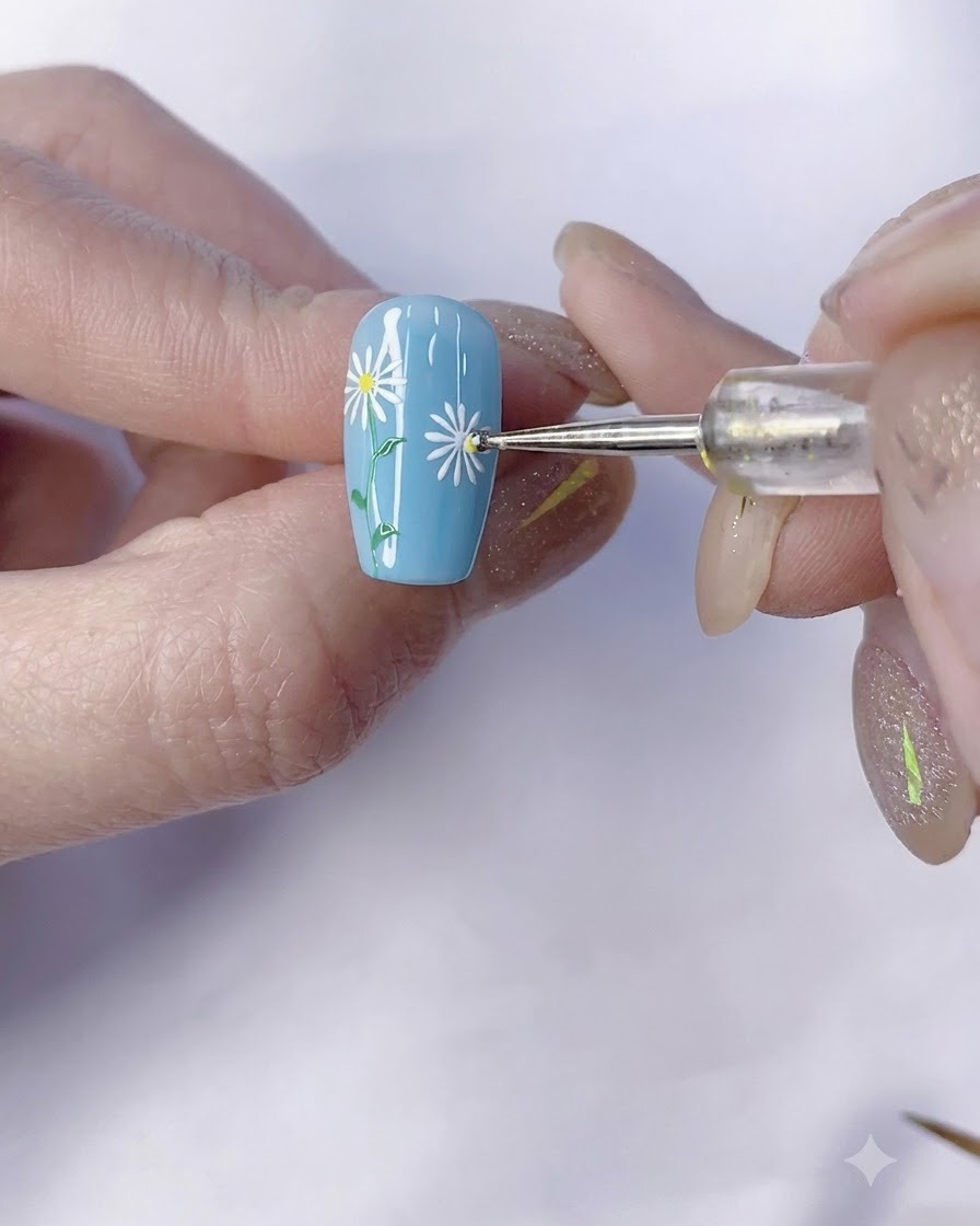Ein Dotting-Tool trägt einen gelben Mittelpunkt auf ein weißes Gänseblümchen auf einem blauen Nagel auf.
