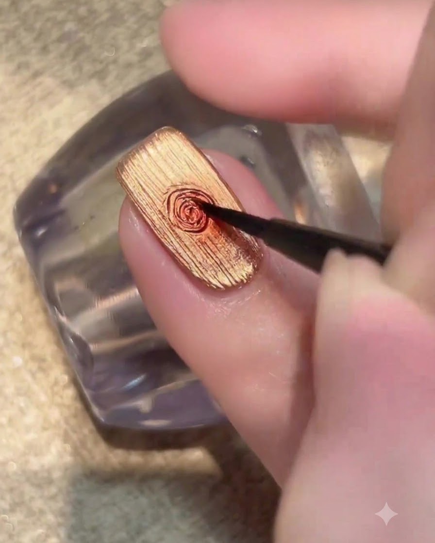 Ein feiner Pinsel platziert einen kleinen Tropfen dunkelroten Gels in der Mitte eines goldenen Nagels.