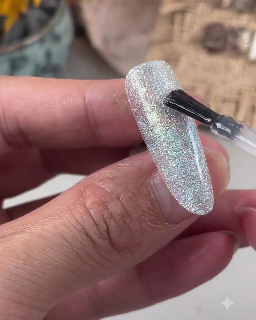 Ein Pinsel trägt klares Niveliergel auf eine glitzernde Nageloberfläche auf.