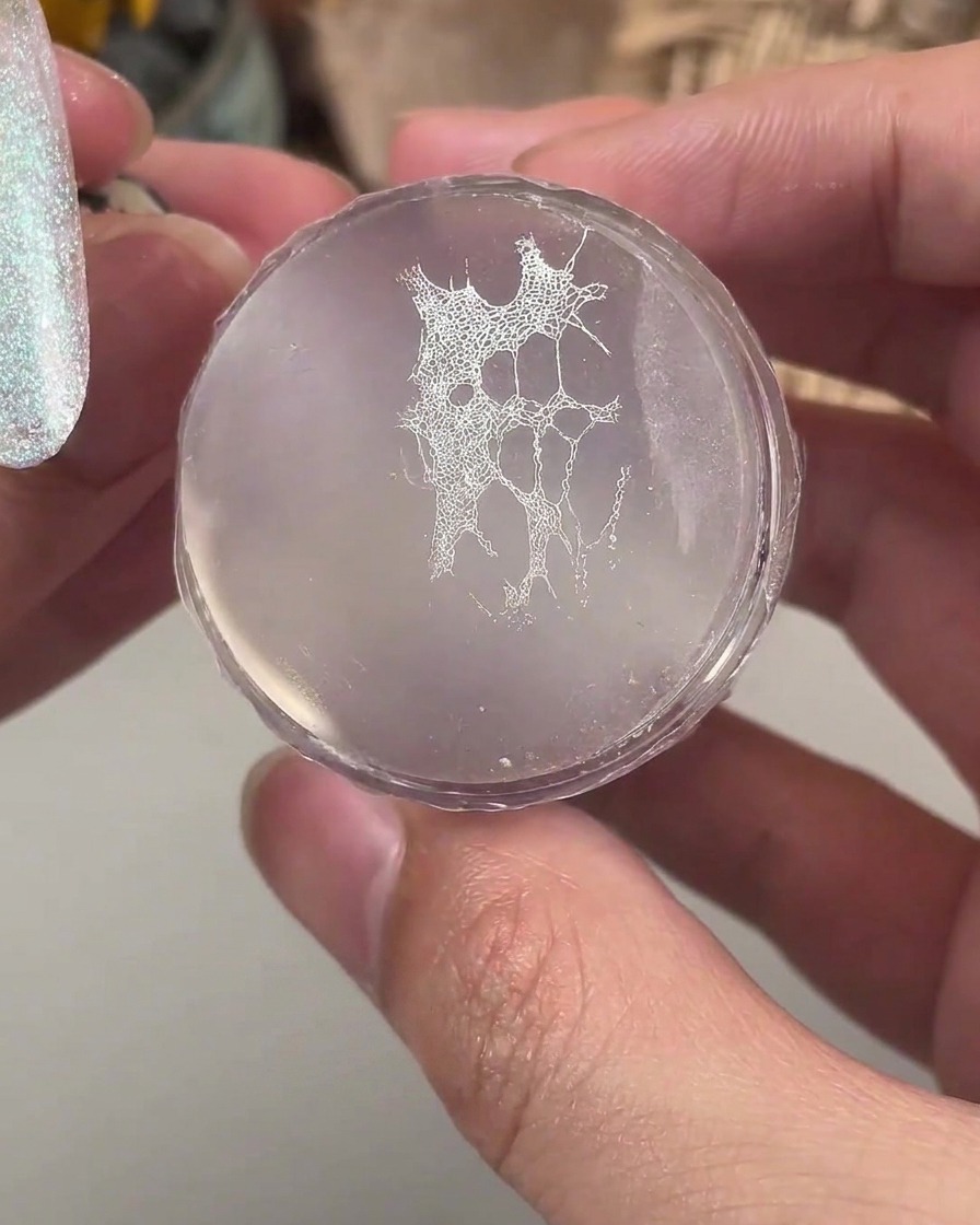 Ein transparenter Silikonstempel hält ein feines weißes Spitzenmuster bereit, das auf einen manikürten Nagel übertragen werden soll.