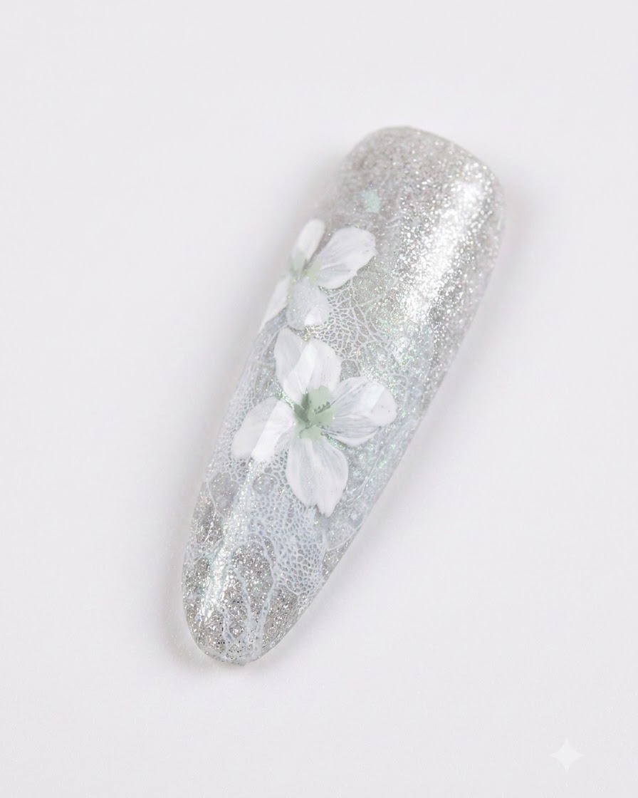 Eine Nahaufnahme eines manikürten Nagels mit zarten weißen Blumen und sanfter grauer Schattierung über einem glitzernden blaugraunen Hintergrund.