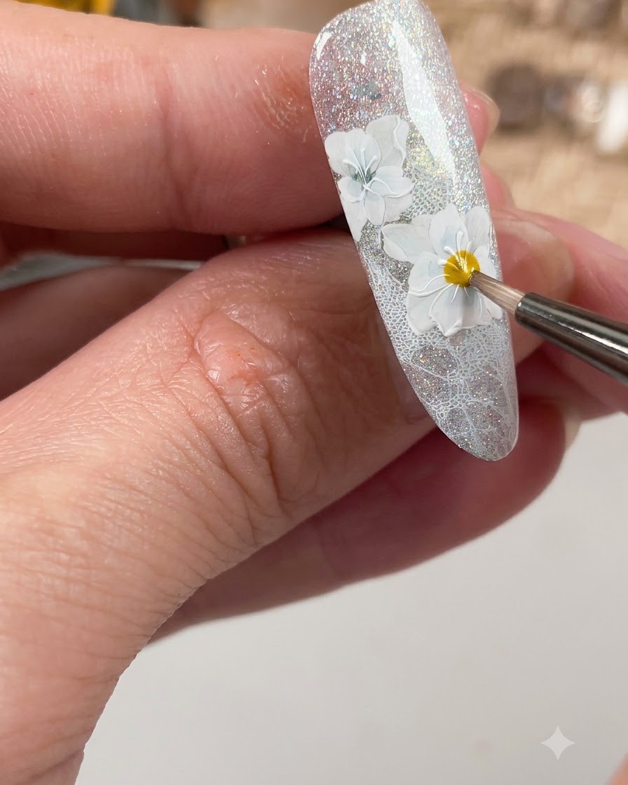 Ein Nagelpinsel trägt einen matten Top Coat speziell über den gestalteten weißen Blumendetails auf dem Nagel auf.