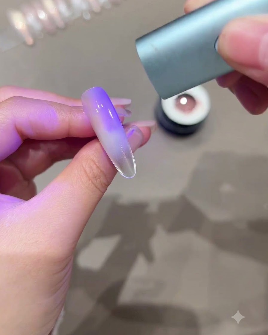 Eine Hand hält eine Mini-UV-LED-Härtungslampe über einen länglichen Nagel mit violettem Cat-Eye-Verlaufeffekt.