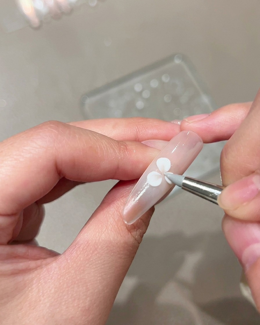 Ein Silikon-Modellierpinsel drückt und formt ein weißes Gel-Blütenblatt auf einem manikürten Nude-Nagel.