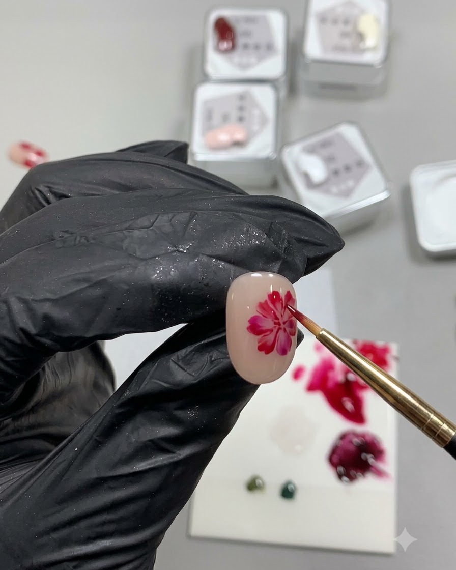 Ein feiner Detailpinsel malt einen weichen, transluzenten, unregelmäßigen roten Kreis, der eine Rosenblattbasis auf einem Nacktnagel darstellt.