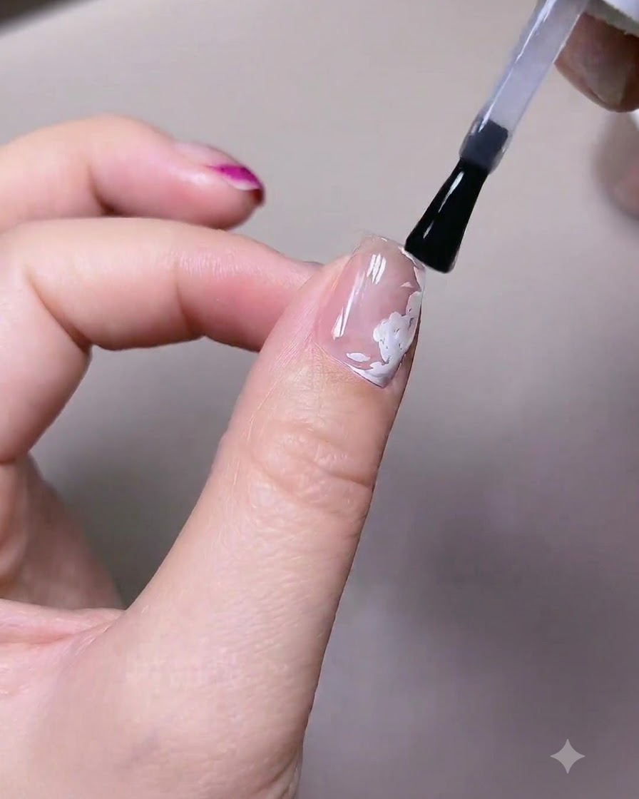 Ein Pinsel trägt eine Schicht matten Top-Gel-Lacks über einen Nagel mit vorgemalten weißen Rosenelementen auf.