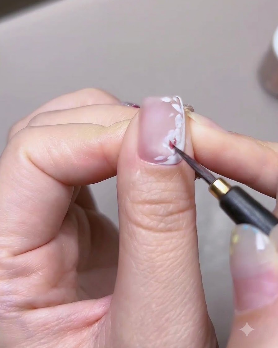 Eine detailreiche Nahaufnahme eines feinen Pinsels, der rote Aquarellfarbe auf die weiße Blütenblattbasis einer Nail-Art-Rose aufträgt.