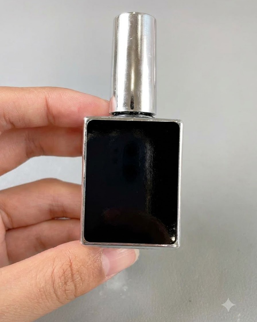 Eine kleine schwarze, rechteckige Flasche Nagellack wird von einer Hand vor neutralem Hintergrund gehalten.