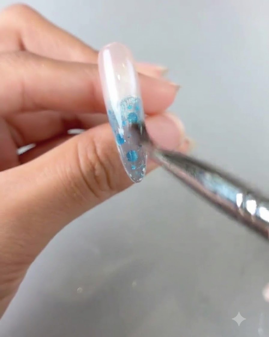 Eine Nahaufnahme eines Pinsels, der blaues Gelprodukt auf einem Nagel verblendet, um einen Ombré-Farbverlauf zu erzeugen.