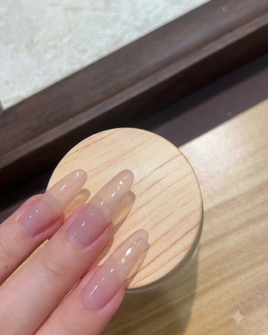 Eine Nahaufnahme langer Nude-Verlängerungsnägel, die mit einer klaren Base-Gel-Schicht vorbereitet werden.