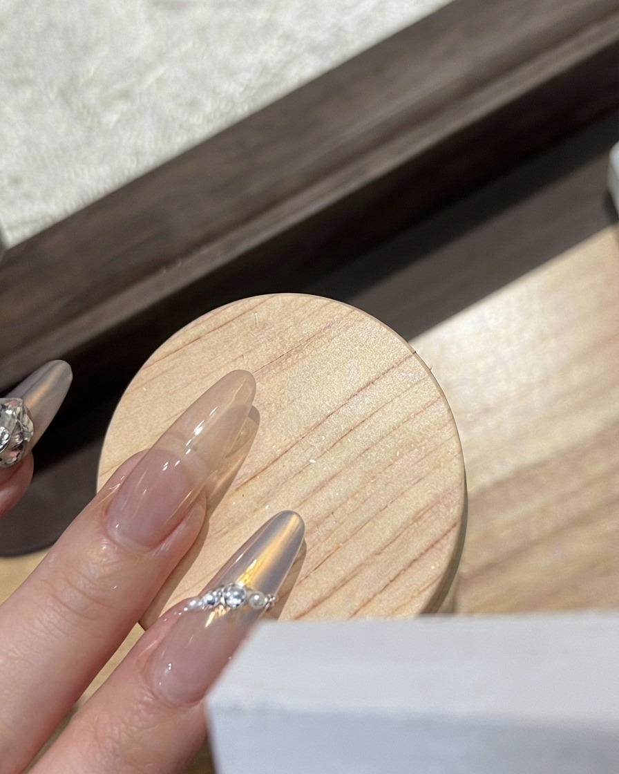 Eine Nageldesignerin platziert einen weißen gefrosteten Schmetterlingsanhänger auf einem glänzenden Nagel.