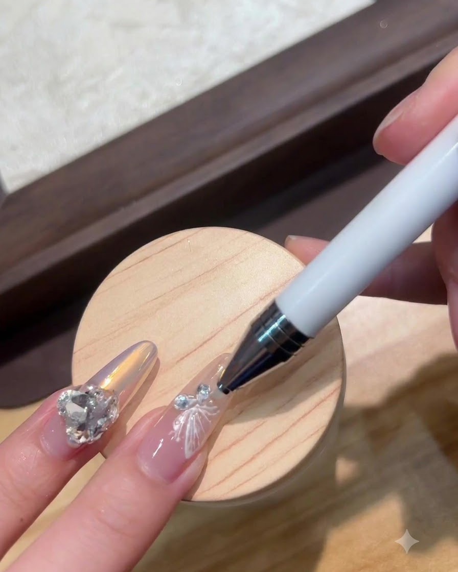 Ein Dotting-Stift platziert einen winzigen Kristall neben einem weißen Schmetterlings-Nagelanhänger.